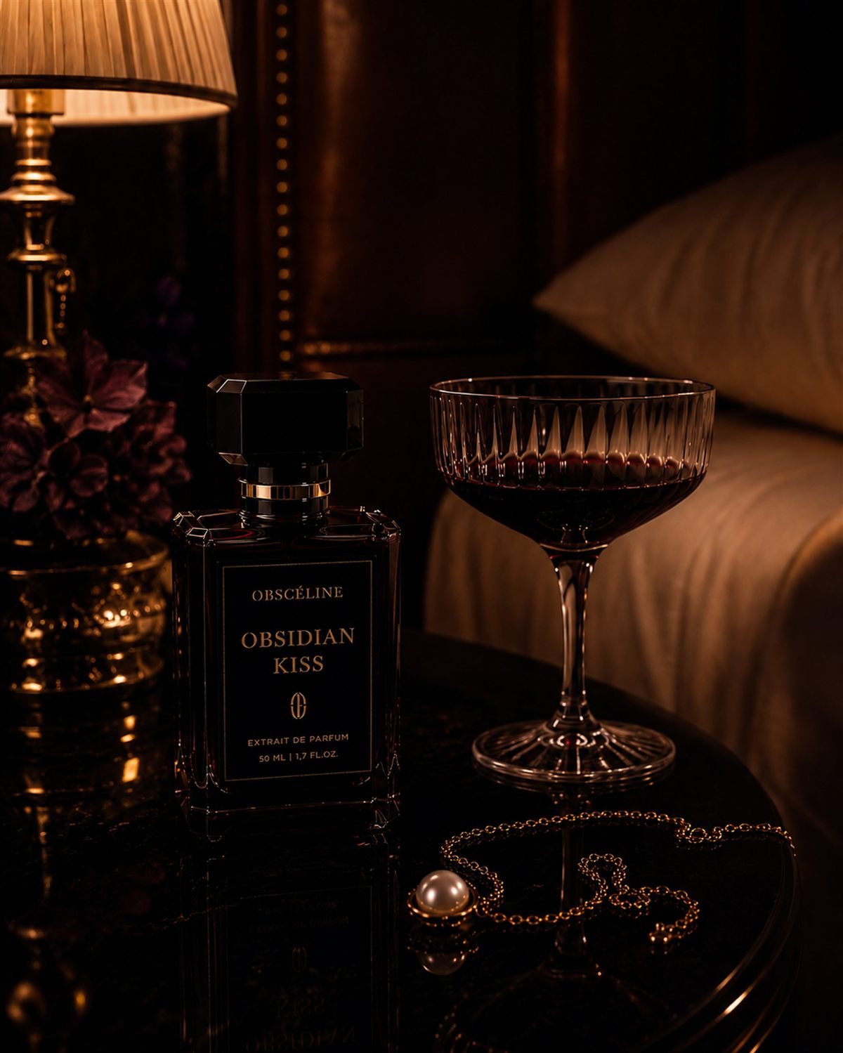 Obsidian Kiss bottle beside a coupe of red wine at night
